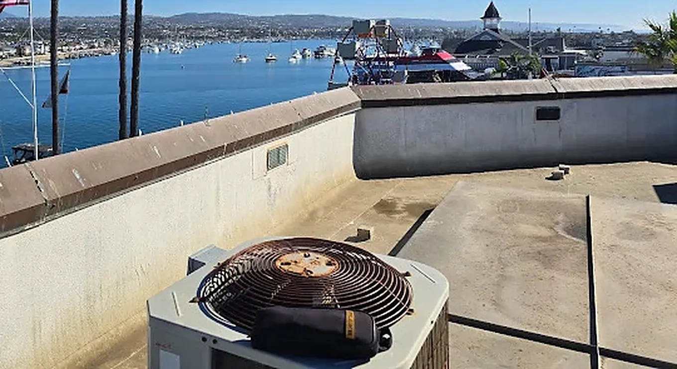 Rust and salt air corrosion visible on the fan grille of a rooftop outdoor condensing unit overlooking Newport Harbor in Orange County