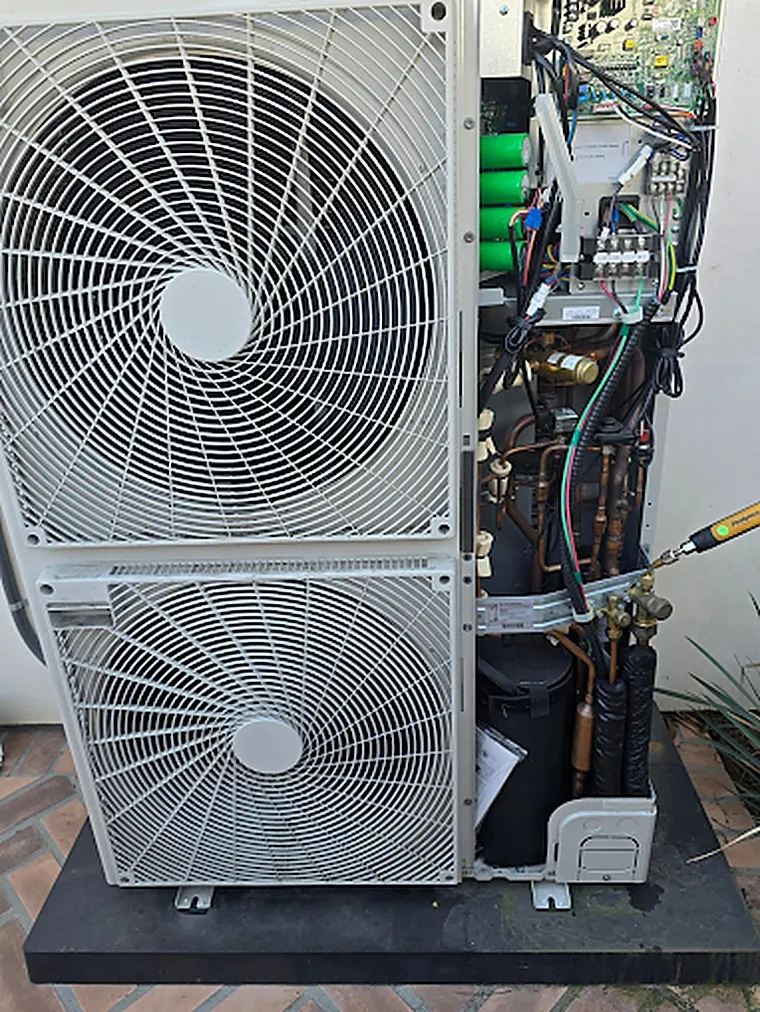 Two-fan inverter heat pump outdoor unit on an elevated pad with its service panel open, showing the control board, copper refrigerant lines and service valves during a Brightwater inspection