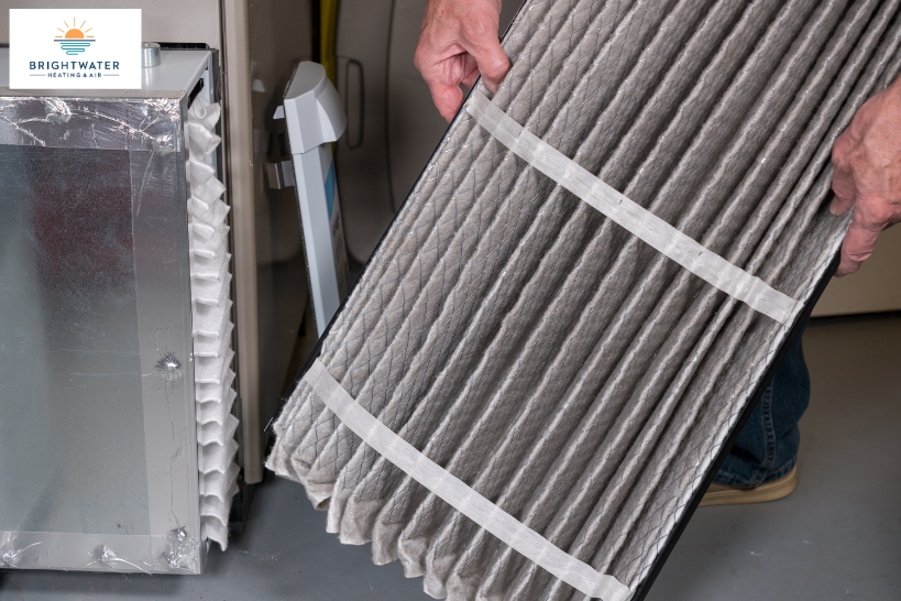 Dirty furnace air filter being removed for replacement during HVAC maintenance.