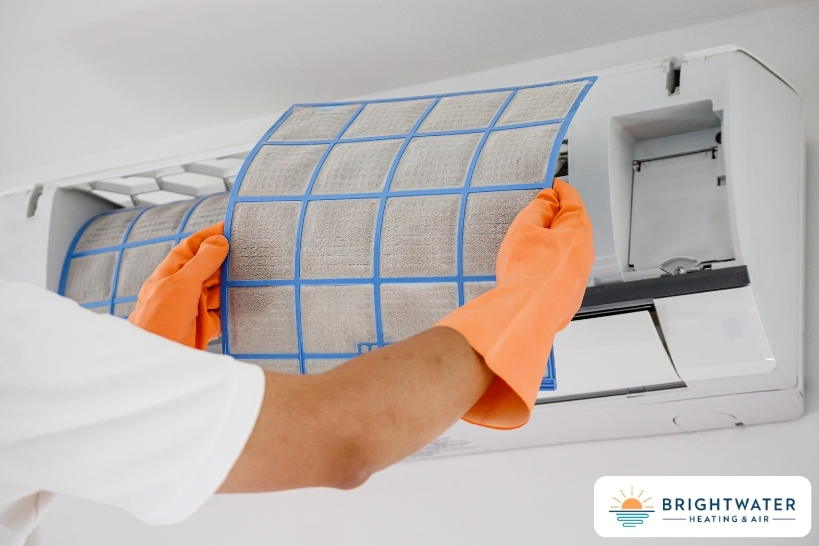 Hands replacing the air filter in a wall-mounted mini split heater unit.